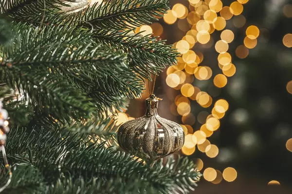 Close-up of branches of a christmas tree with a glass toy on a golden background of glowing garlands