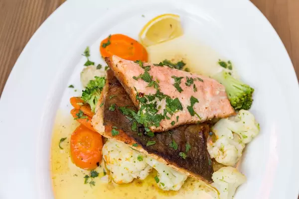 Close-up of char on a white plate, served with veggies, herbs and sauce. Fish recipe from the Alps