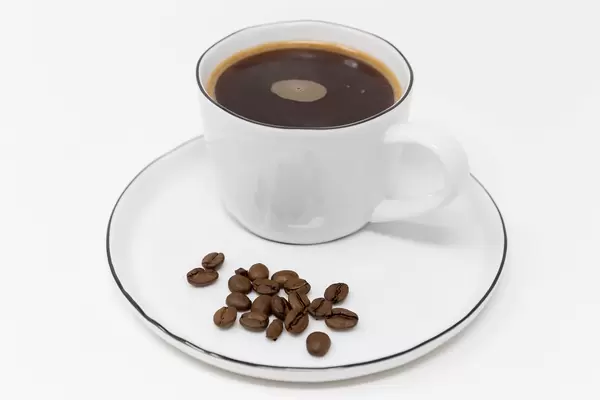 Close-up of coffee beans on a white plate with a black coffee in a white cup as an energy boost