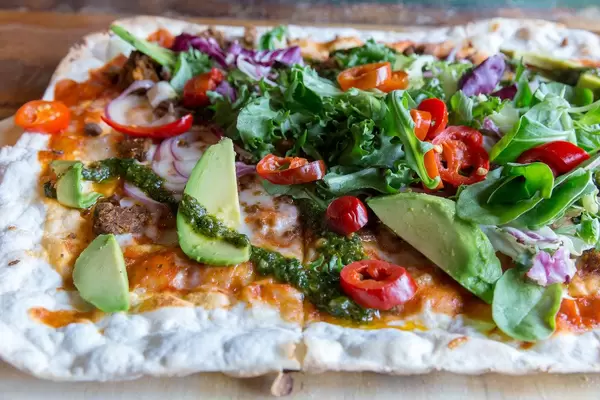 Close-up of colorful Flatbread with vegan chili-härkis made of horse beans, avocado, salat, tomatoes, red onions, tomato sauce and chimichurri