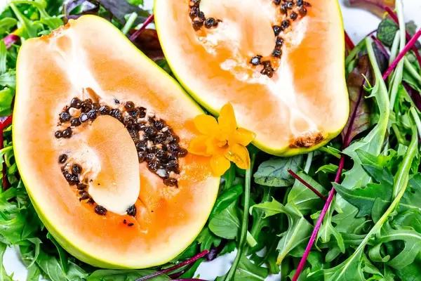 Close-up of cut papaya with yellow flower and mixed leaves