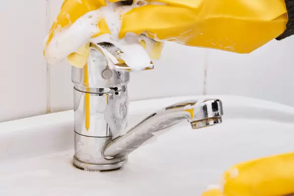 Close-up of female hands with protective gloves scrubbing and cleaning bathroom faucet