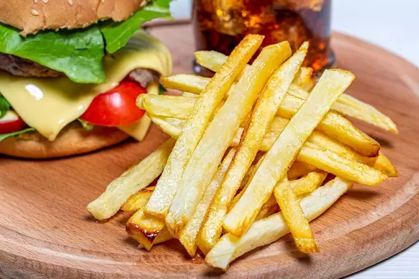 Close - up of fried potatoes, behind him a Burger and a glass of coke