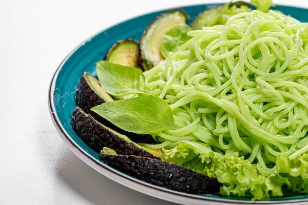 Close up of green spaghetti with avocado slices and basil