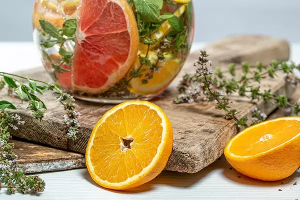 Close-up of half oranges, fresh mint and a jug of lemonade