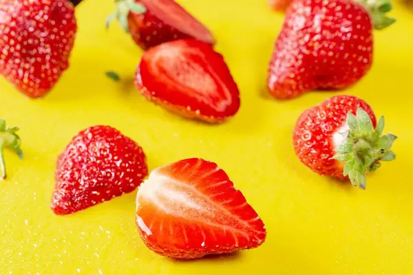 Close-up of halves and a whole strawberry with yellow background