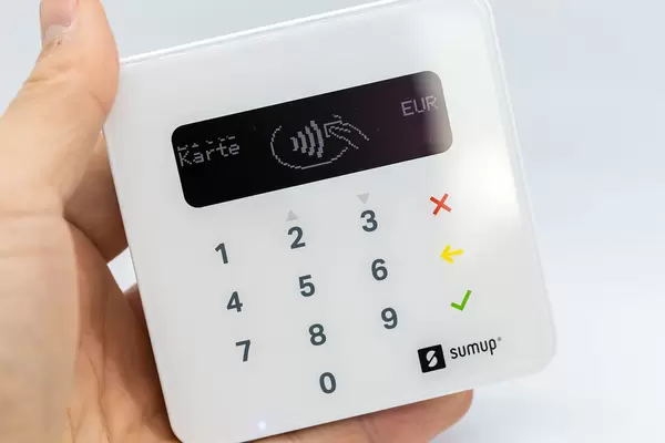 Close-up of hand holding a white SumUp Air Card Reader: portable device for contactless payments