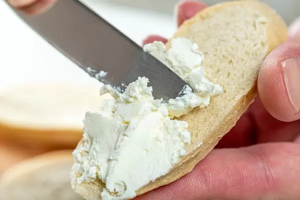 Close-up of hand spread cheese on bread with a knife