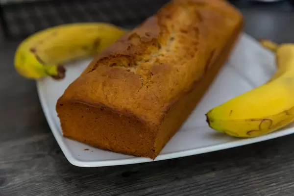 Close-up of homemade banana bread with brown crust, on a white plate, on a wooden table
