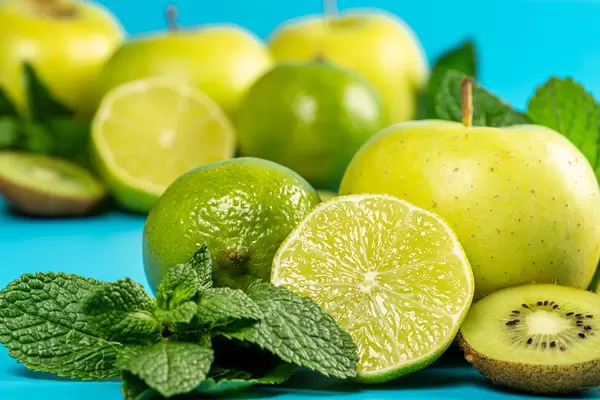 Close-up of lime, kiwi, apple and mint leaves on blue background