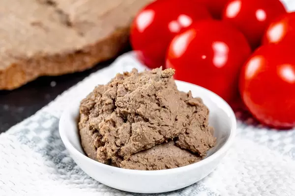Close-up of liver pate in white bowl with tomatoes behind