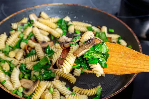 Close-up of pasta, mushrooms, herbs and spices on a wooden kitchen spatula