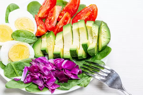 Close-up of pieces of avocado, purple cabbage, tomato with spinach and half boiled eggs
