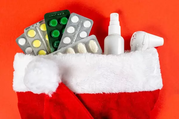 Close-up of pills, thermometer and antiseptic in santa hat on red background