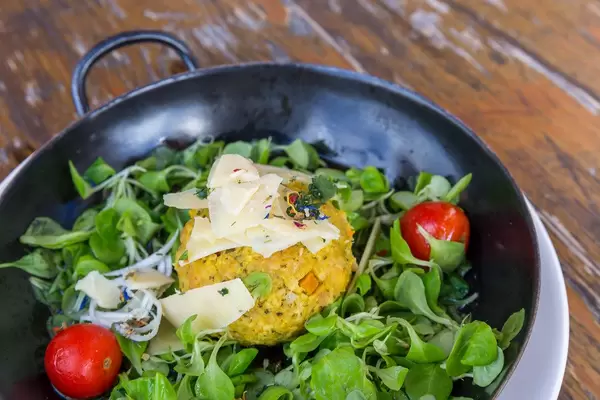 Close-up of pumpkin Knödel (dumpling) in a pan with salad and parmesan cheese slices in Alpbach