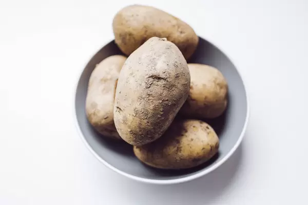 Close up of raw potatoes in a bowl. White background.