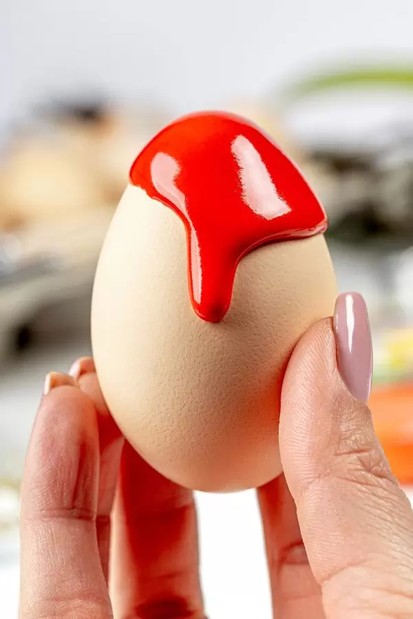 Close-up of red paint flowing down a chicken egg in a female hand (Flip 2020)