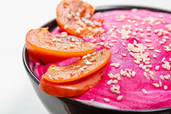 Close-up of slices of persimmon and sesame seeds on pink yogurt. Beautiful oatmeal for Breakfast