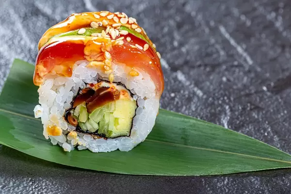 Close - up of sushi rainbow dragon on a green leaf on a black background