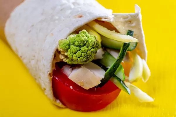 Close-up of vegetables and meat wrapped in pita on yellow background (Flip 2019)