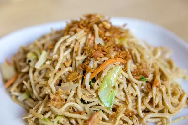 Close-up of vegetarian Asian noodles, fried vegetables and egg sauce, on a white plate on a wooden table