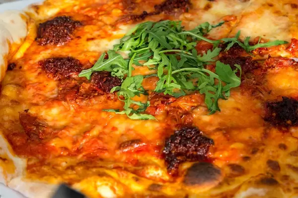 Close-up of Vegetarian piquant Pizza NDUJA CALABRESE at "LOsteria", with rucola, mozzarella, ital. Spread salami and semi-dried cherry tomatoes