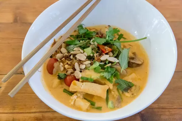 Close-up of Vietnamese meal with chopsticks: Vegan organic tofu in red coconut curry sauce with cherry tomatoes, baby eggplant, fried onions & peanuts