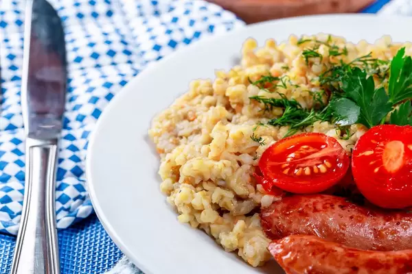 Close-up of wheat porridge with sausages on a white plate
