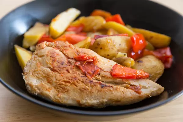 Close up on chikcen breast with baked potatoes and red peppers