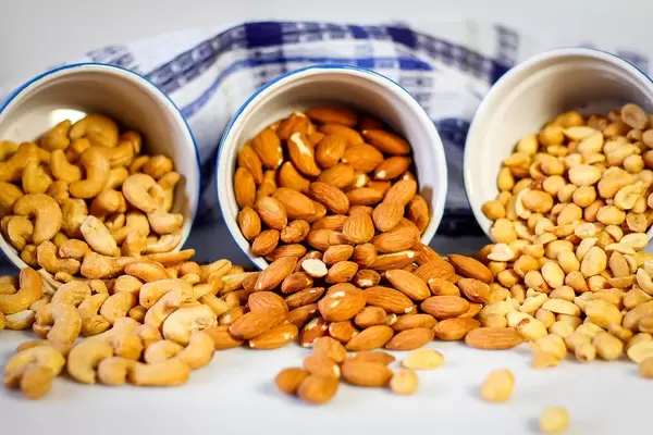 Close Up Photo of Cashew Nuts, Almonds and Peanuts falling out of three Bowls