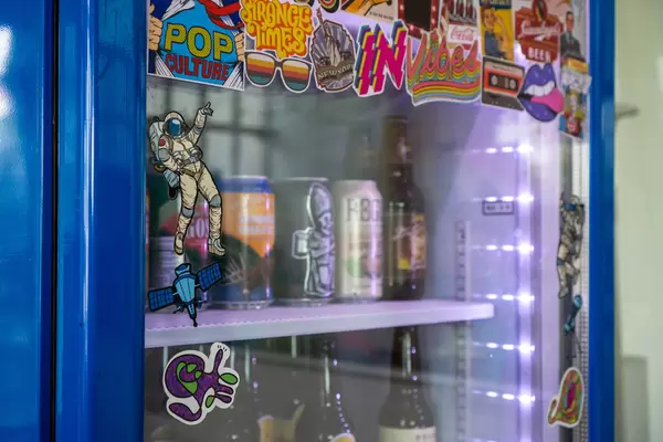 Close Up Photo of Dancing Astronaut Sticker on a Beverage Fridge with Beer Cans and Bottles inside