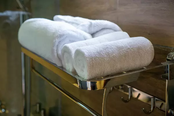 Close Up Photo of Large Bath Towels and Small Face Towels on a Towel Rack in a Hotel Bathroom with Shower in the Background