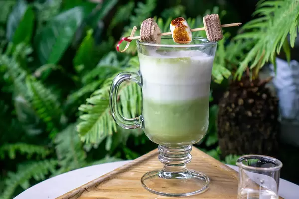 Close Up Photo of Latte Macchiato in a Coffee Glas topped with Roasted Marshmallow and Cookies on a Skewer on a Balony of a Coffee Shop