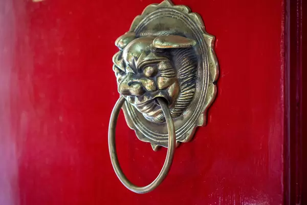 Close Up Photo of Metal Door Knocker in Shape of a Chinese Guardian Lion with Large Ring on a Red Wooden Door of Phuc Kien Pagoda in Hoi An, Vietnam