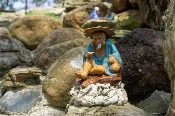 Close Up Photo of Painted Miniature Figure of an Asian Old Man sitting on a Rock in the Garden of Sound of Silence Coffee at An Bang Beach in Hoi An, Vietnam