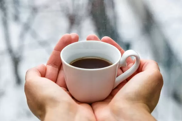 Close Up Photo of Person holding a Small White Cup of Coffee in both Hands with Blurry Background