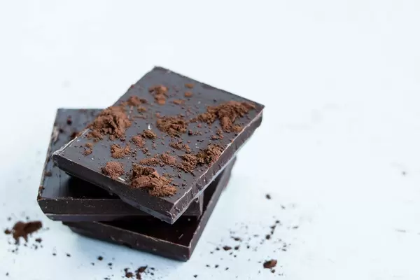 Close Up Photo of Pieces of Dark Chocolate stacked on each other with Cocoa Powder on white Background