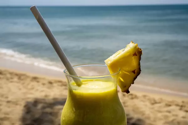 Close Up Photo of Pina Colada with Fresh Pineapple and Paper Drinking Straw in a Cocktail Glass with Beach and Sea in the Background