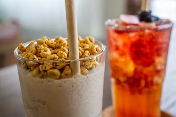 Close Up Photo of Puffed Rice Cereals as a Topping on a Cookies and Cream Milkshake with Paper Straw with Strawberry Ice Tea in the Background