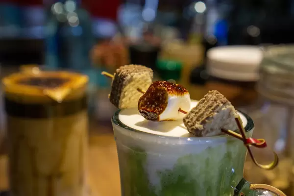 Close Up Photo of Roasted Marshmallow and Cookies on a Skewer on top of a Glas with Milk Coffee in a Cafe