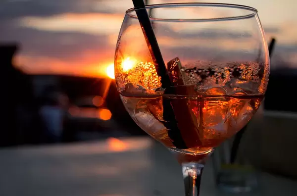 Close Up Photo of Spritz Veneziano Cocktail with Plastic Straw and Slice of Lime with Sunset in the Background
