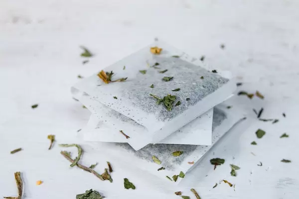 Close Up Photo of Stack of Tea Bags with Dried Tea on and around it on White Background