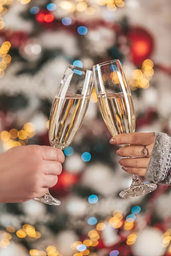 Close up, photo of two people holding glasses of champagne on xmas bokeh background