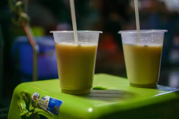 Close Up Photo of two Plastic Cups of Hot Soy Milk on a Green Plastic Stool
