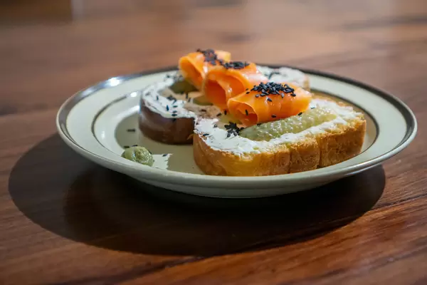 Close Up Photo of two Slices of White Bread with Cream Cheese, Pickled Cucumbers, Smoked Salmon, Sesame and Horseradish on a Plate