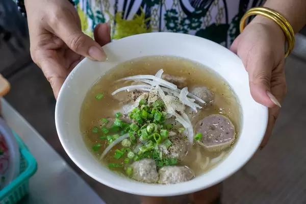 Close Up Photo of Vietnamese Street Food Seller holding a Bowl of Fresh Pho Bo with Beef Balls, Onions and Spring Onions