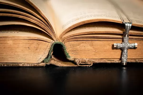 Close Up Photo of Vintage Old Open Bible with Silver Cross as Bookmark