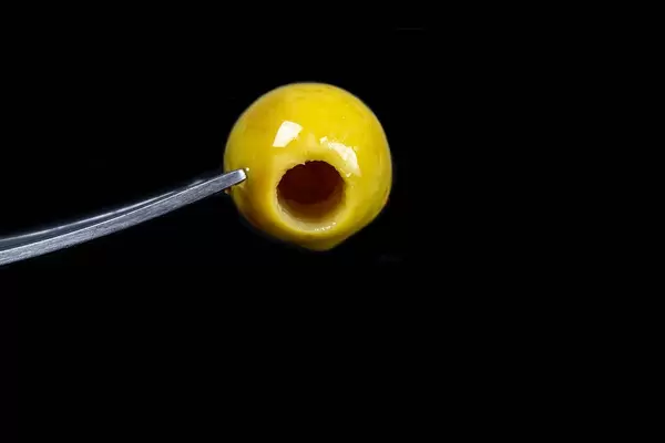Close-up, pickled green seedless olive on a black background with a fork