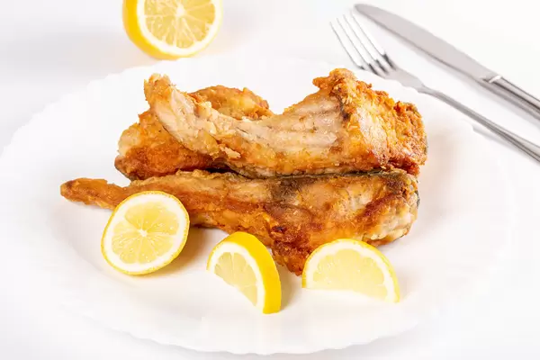 Close-up, pieces of fried fish and lemon on a white plate