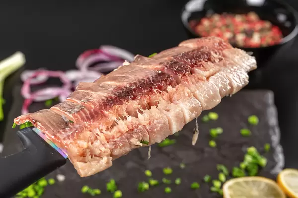 Close-up, pieces of salted herring fillet on a knife